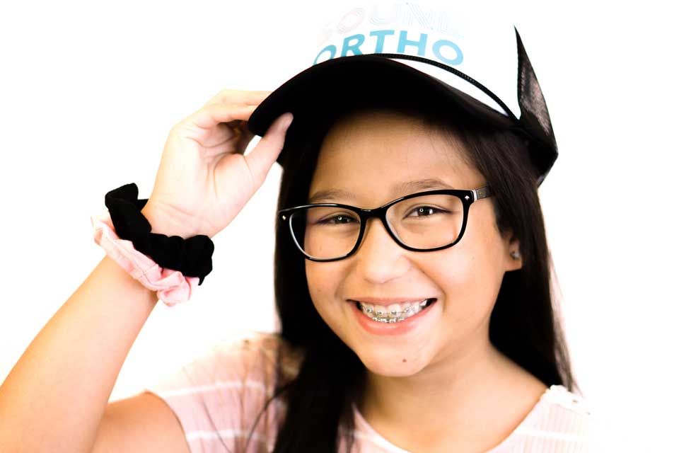 Girl smiling wearing braces glasses and a baseball hat